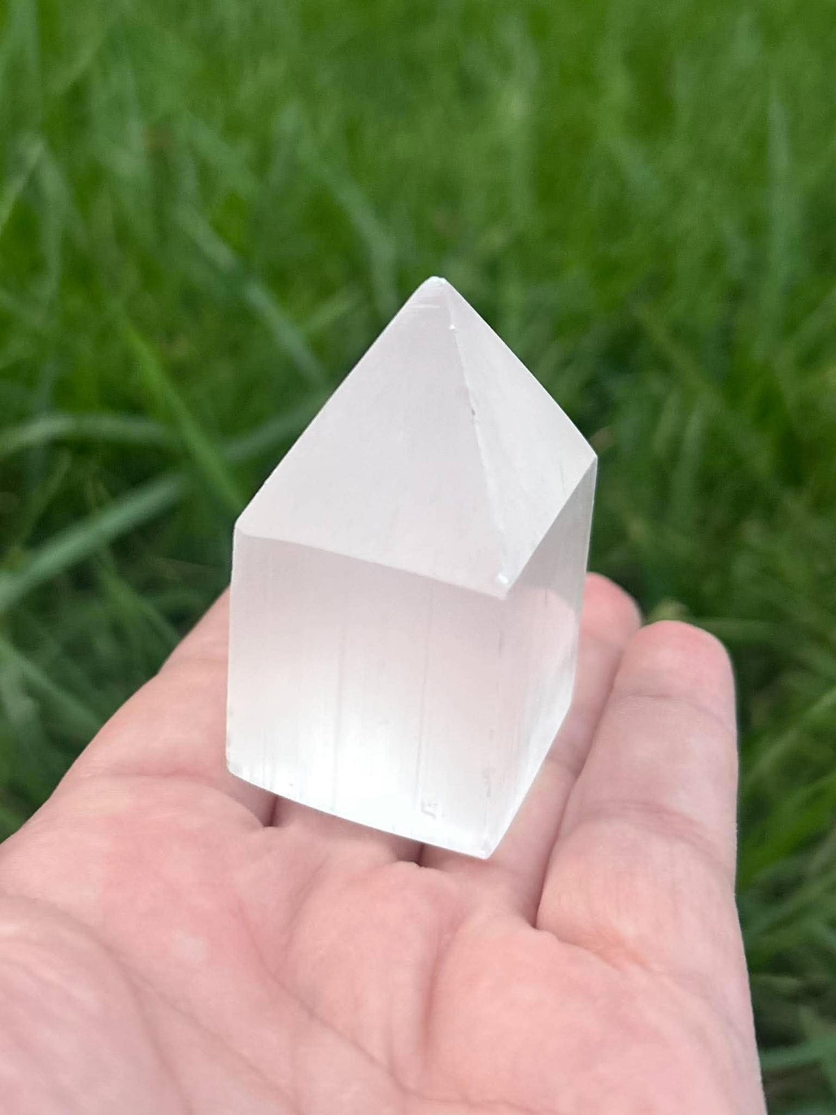 Hand holding polished selenite crystal tower showing size and translucency