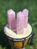 Three polished Rose Quartz crystal towers with soft pink coloring displayed outdoors on a drum