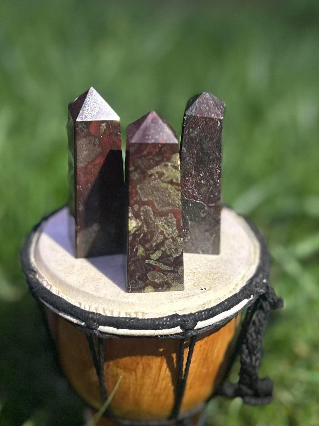 Three polished Dragon Blood Jasper crystal towers with natural deep green, red and burgundy patterns outdoors