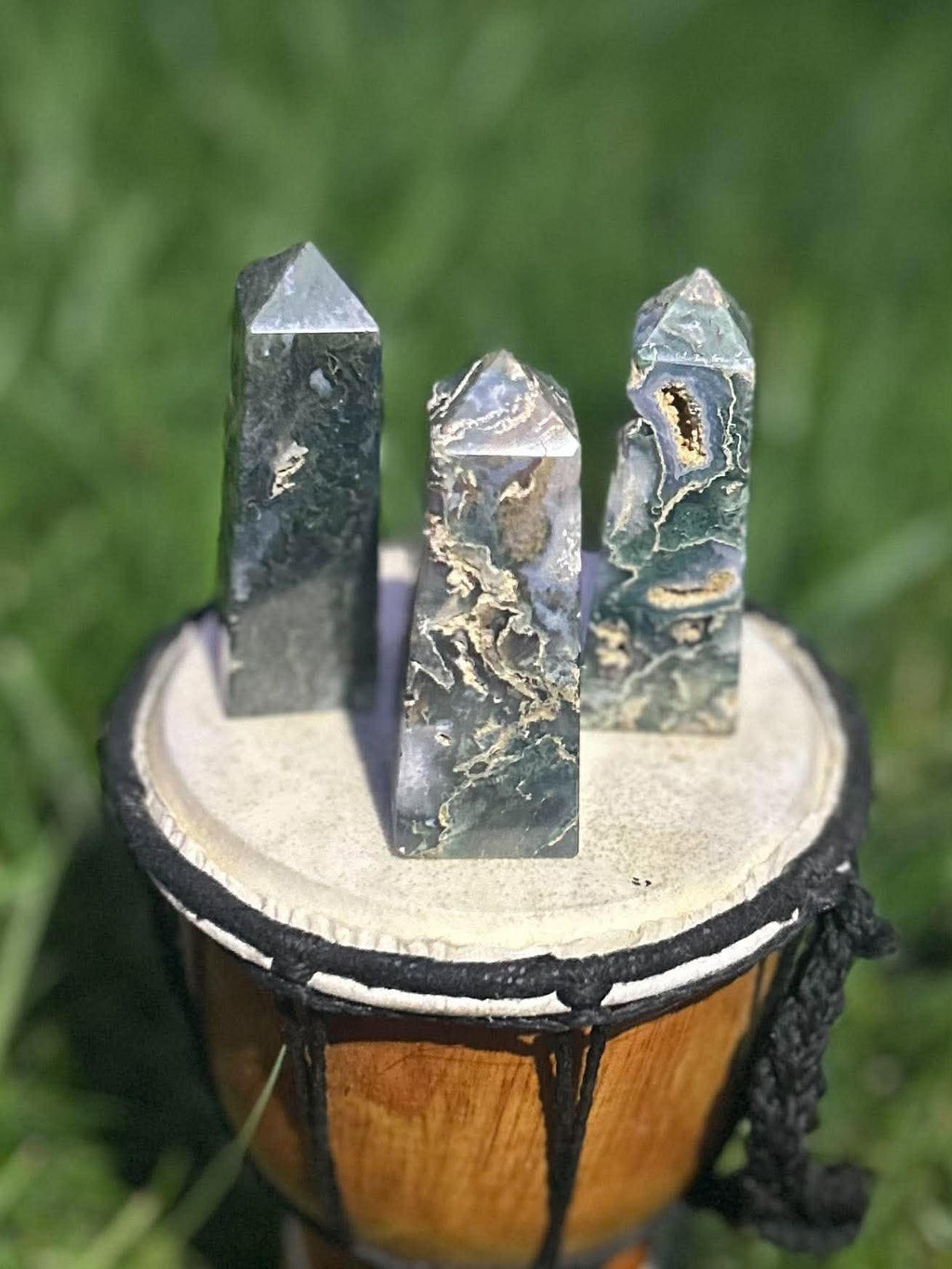 Three polished Moss Agate crystal towers with green, gray and cream natural patterns displayed outdoors