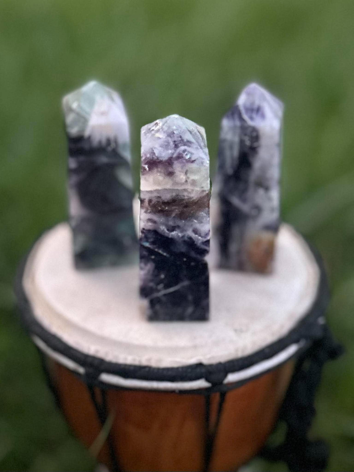 Three Rainbow Fluorite crystal towers with natural purple, green and clear banding displayed outdoors