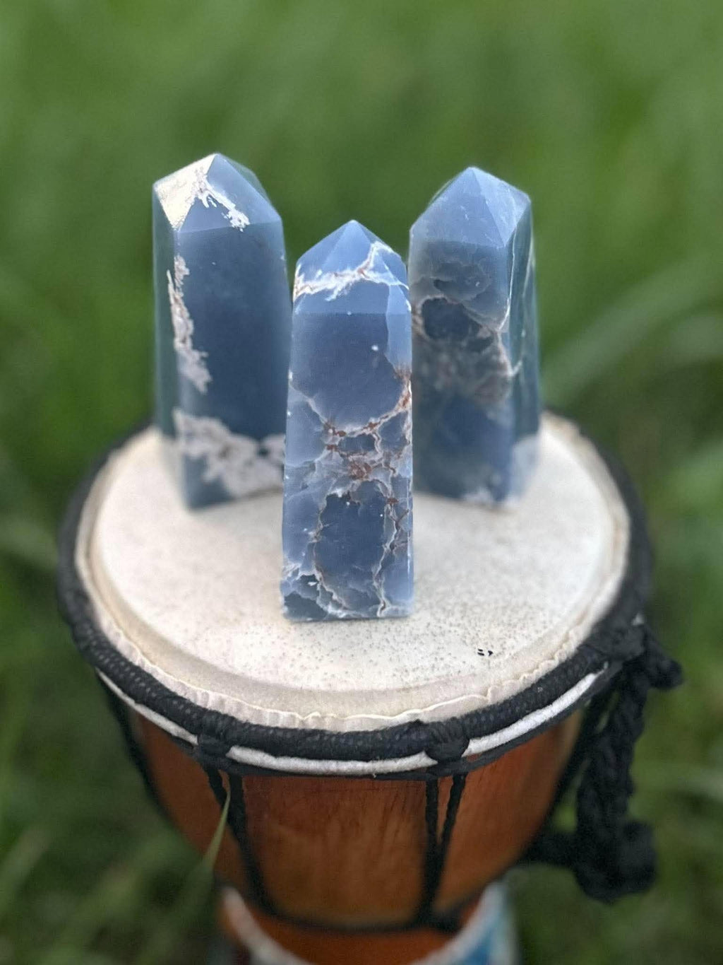 Three blue Angelite crystal towers with natural matrix displayed outdoors on a drum