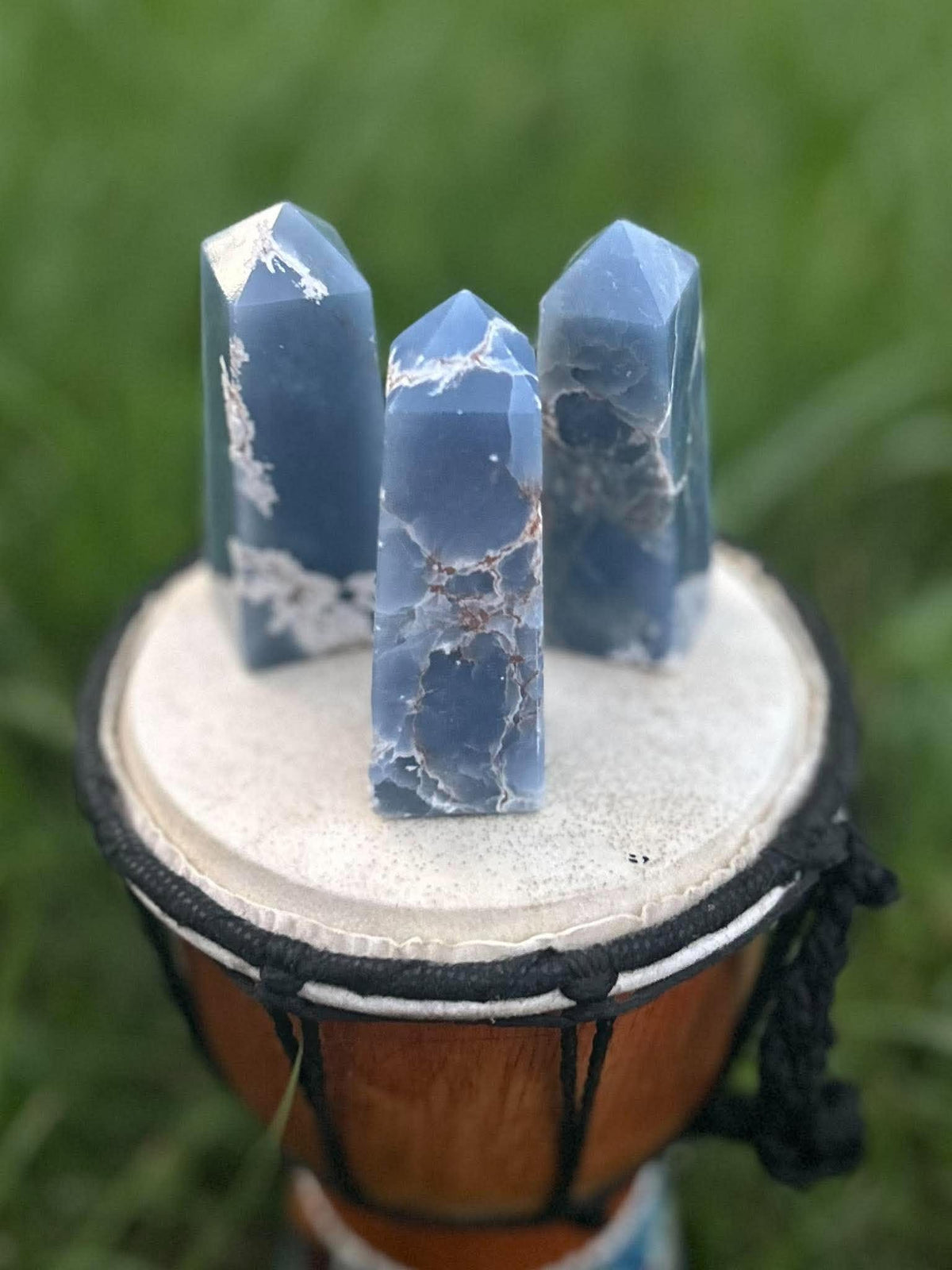 Three blue Angelite crystal towers with natural matrix displayed outdoors on a drum