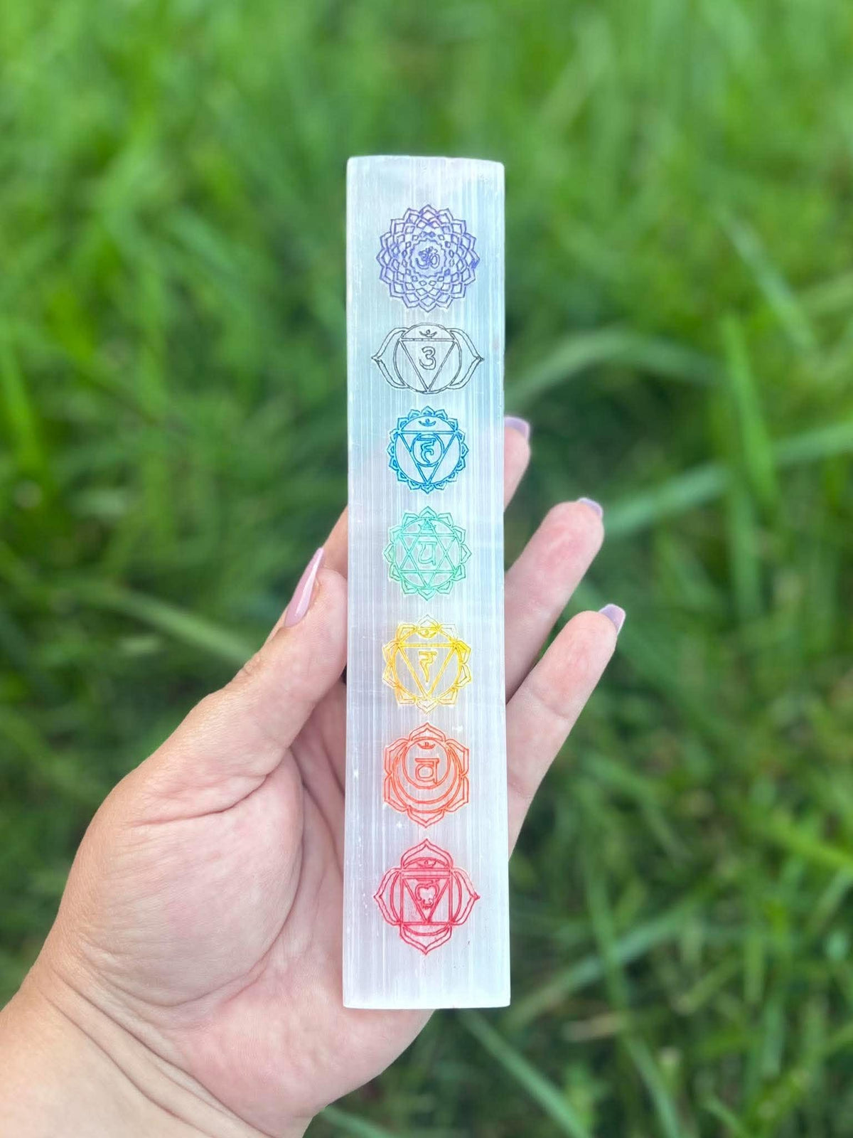 Hand holding selenite chakra charging plate with seven colored chakra designs