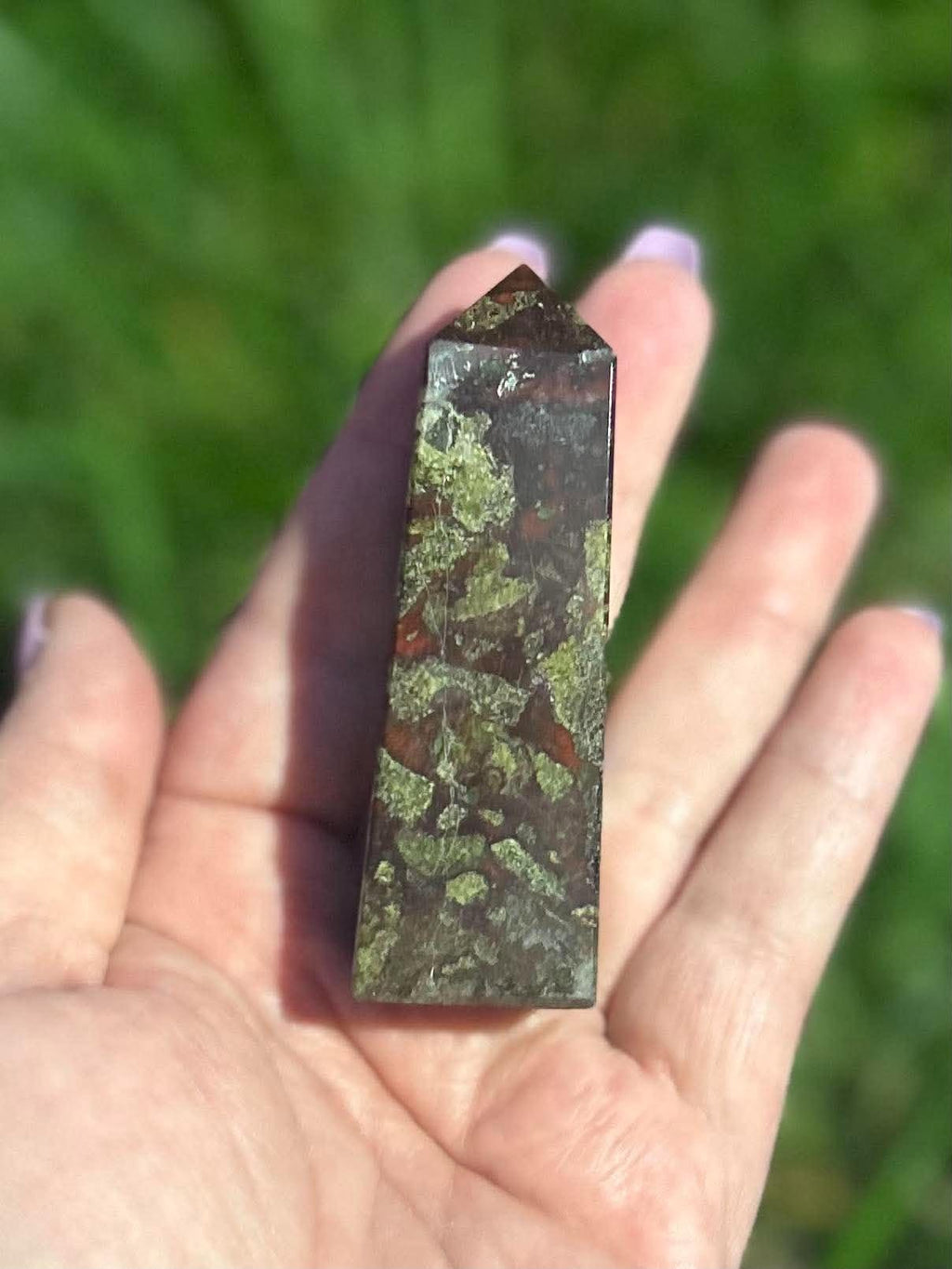Polished Dragon Blood Jasper tower held outdoors showing detailed green, burgundy and earthy natural patterns
