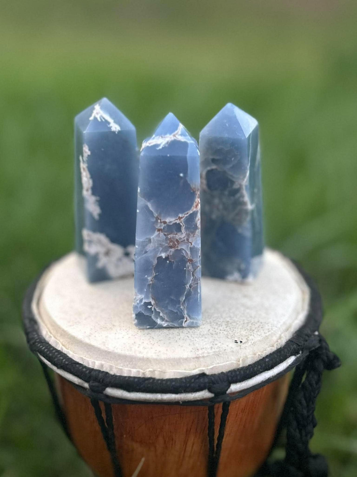 Three natural blue Angelite crystal towers displayed on a drum outdoors