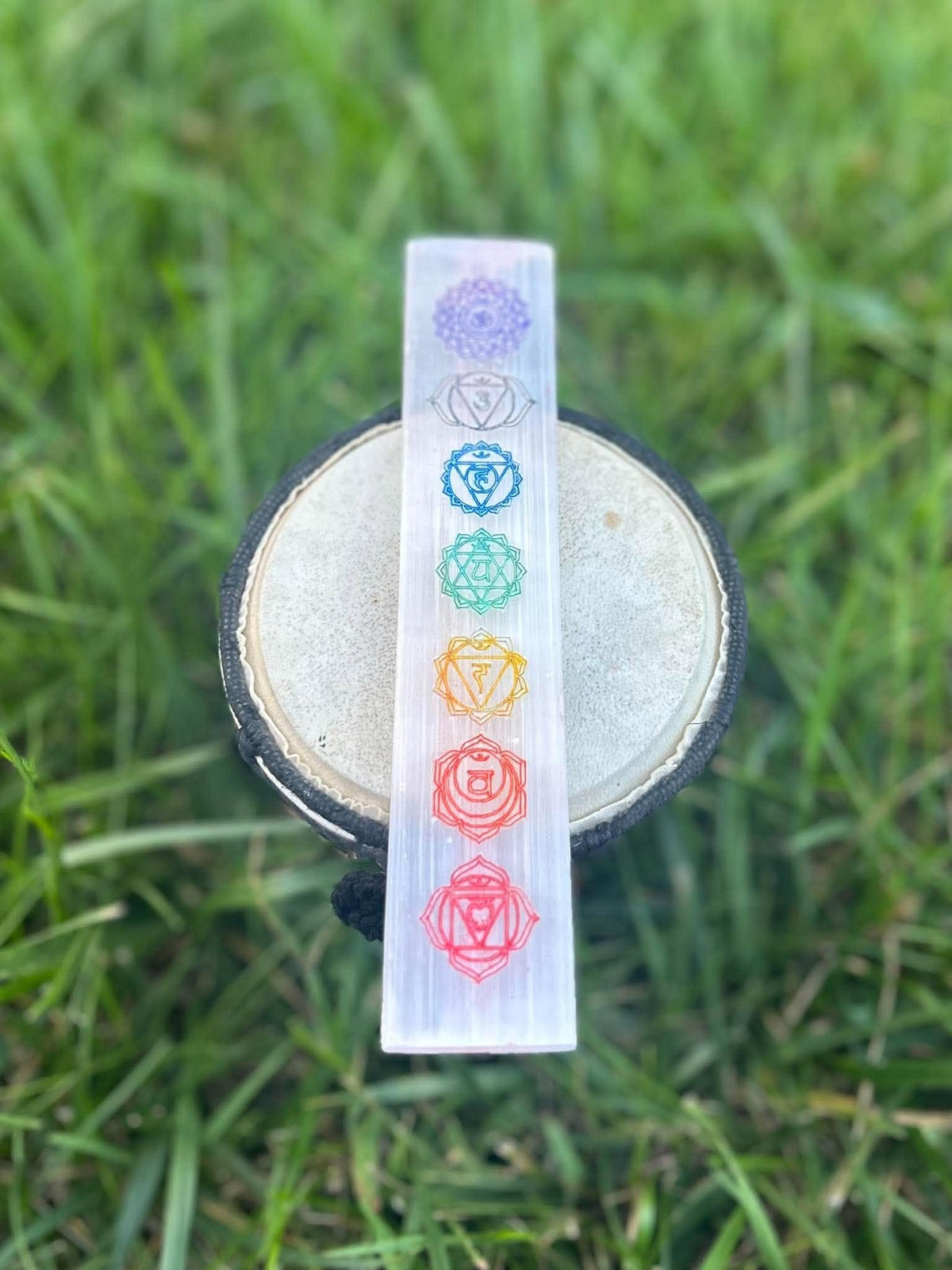 Seven chakra selenite charging wand displayed upright on a drum