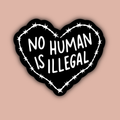 Heart-shaped sticker with 'No Human Is Illegal' text on a pink background